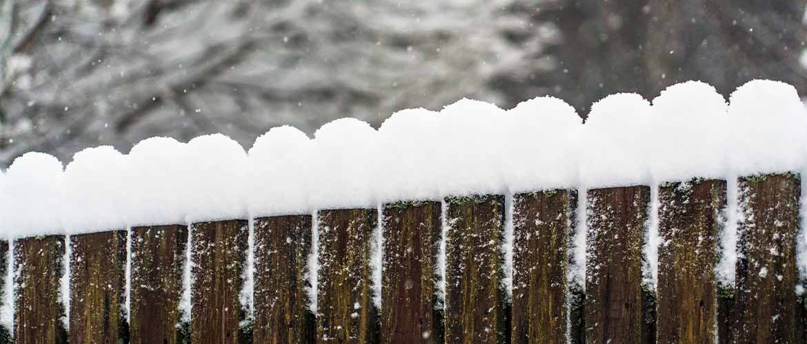Snow falling and collecting on top of wood fencing.